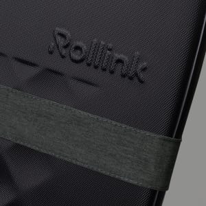 A close-up of a black suitcase featuring a textured surface and an attached dark green strap. It has a logo visible.