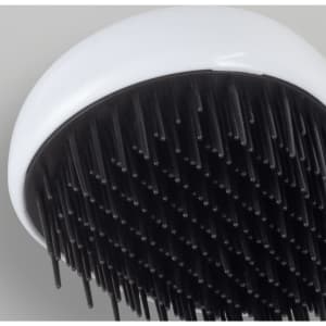 A hair detangler brush with a white handle and black bristles, featuring a round design.