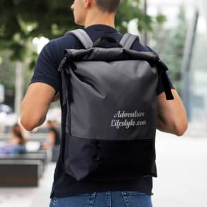 A person wearing a grey and black Fjord Backpack, with a logo on the back, standing outdoors.