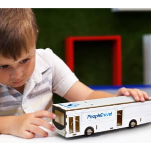 A white wooden bus model is being examined by a child, featuring a branding logo on the side.