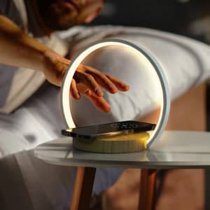 A white wireless charging night light with a circular design, illuminating a smartphone on a wooden table.