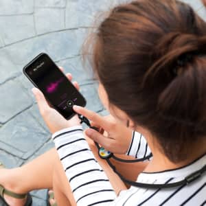 A person holds a black smartphone attached to a lanyard, with a colourful logo, against a textured surface.