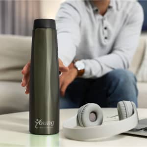 A drink bottle in a sleek, dark green colour with a logo, placed on a table beside headphones.