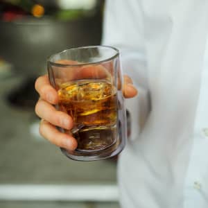 A drink bottle made of double wall glass, featuring a clear design with a brown liquid inside, held in a hand.