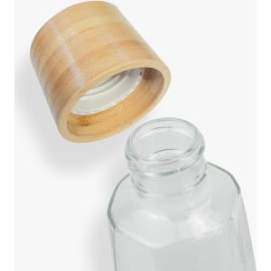 A glass drink bottle with a bamboo lid. The bottle has an octagonal shape and is transparent.