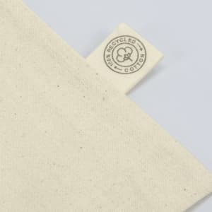 A cream-coloured tote bag made from recycled cotton, featuring a tag with a logo.