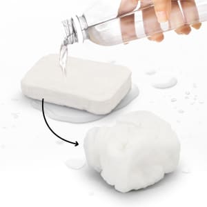 A small compressed towel in white, next to a hand pouring water from a clear drink bottle.