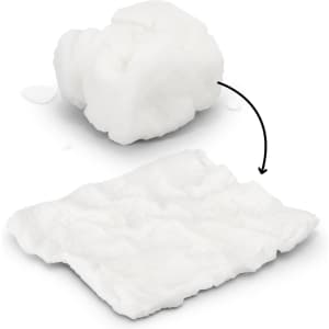 A compressed white towel, transforming from a small compact shape to a flat, textured cloth, with water droplets nearby.