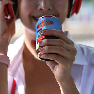 A drink bottle held by a person wearing headphones, featuring a blue design and a logo.