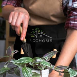 A person using a black trowel with a wooden handle, wearing an apron with a logo, tending to a potted plant.