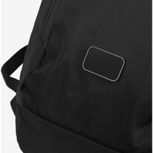 A black roll-up backpack with textured fabric and a small branded patch. The straps are visible on the side.