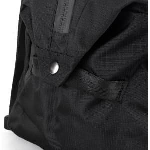 A close-up of a black duffle bag featuring fabric texture and a snap button closure. It has a logo on the side.