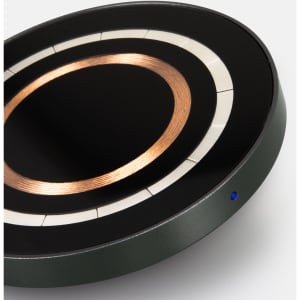 A wireless charger in black and green, featuring a copper circle design and a small blue indicator light.