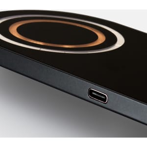A sleek black wireless charger features a circular charging area in gold. Includes a USB-C port.