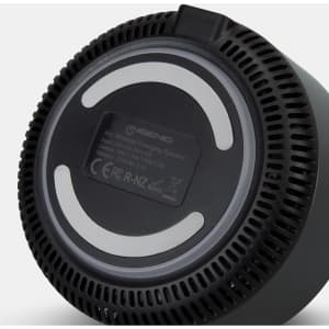 A wireless charging speaker with a round base, featuring a smooth black surface and a vented design. It has a branding logo.