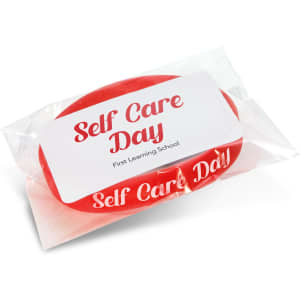 A red silicone wristband packaged in plastic, featuring a label with the words "Self Care Day" and a logo.
