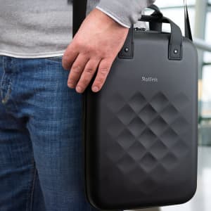 A black Rollink Laptop Case with a textured design, being held by a person wearing jeans and a grey sweater.