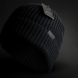 A black beanie with a ribbed texture and a tag attached, featuring a logo.