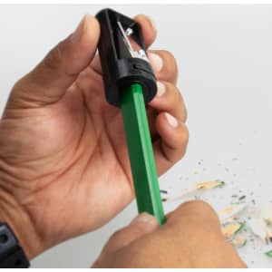 A black and grey pencil sharpener being used on a green carpenter’s pencil, surrounded by wood shavings.