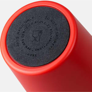 A red coffee cup with a round black base, featuring a logo and instructions for use.