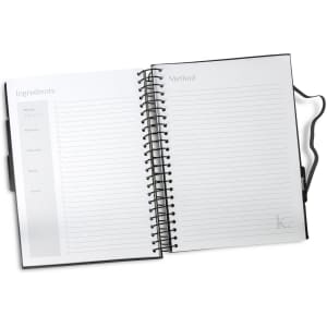 A black, spiral-bound recipe journal with blank pages for ingredients and method sections. It has a logo on the cover.