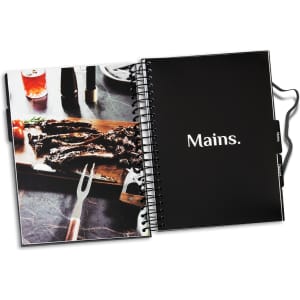 A black spiral-bound recipe journal with a photo of grilled meat on a wooden board and a fork.