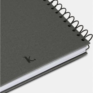 A grey spiral-bound journal with a textured cover and a simple black logo on the bottom corner.