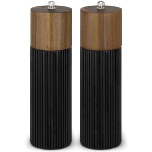A pair of salt and pepper grinders with wooden tops and ribbed black bases. Each grinder has a silver knob on top.