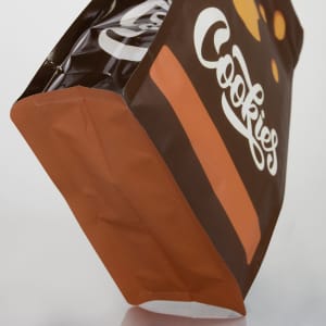 A small foil flat bottom pouch in black and orange with a logo, designed to hold snacks or cookies.