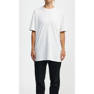 A white essential T-shirt, with short sleeves, displayed on a model, paired with black trousers. The shirt has a branding logo.