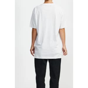 A white t-shirt with short sleeves is displayed on a person from the back, paired with black trousers. The shirt features a logo.