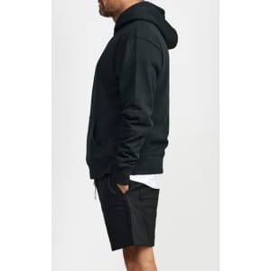 A black hoodie worn by a man, featuring a front pocket and a hood, paired with black shorts.