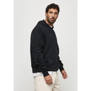 A black hoodie with a front pocket and a hood, displayed on a model standing sideways. Includes a logo.