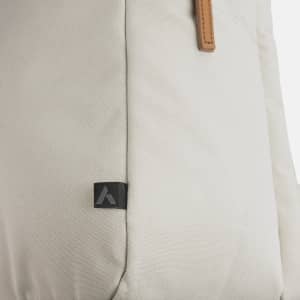 A beige backpack with a textured surface and leather accents, featuring a small logo on the side.