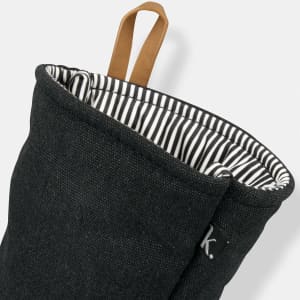 A dark grey oven mitt with a striped interior and a leather loop for hanging. It features a small logo.