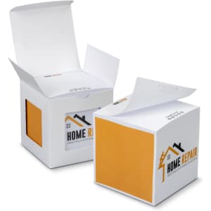 A sticky cube in white and orange, featuring a logo, with two boxes partially opened. Each box contains multiple sticky sheets.