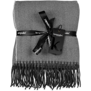 A grey herringbone throw blanket wrapped with a black ribbon and tag, featuring fringed edges.