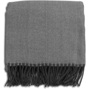 A grey herringbone throw blanket with fringe detailing, neatly folded. It has a subtle pattern and a soft texture.