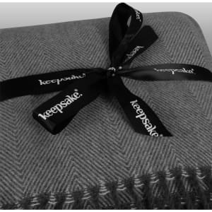 A grey patterned throw blanket tied with a black ribbon featuring a logo.
