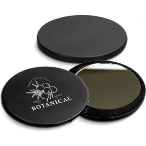 A round black compact mirror with a reflective interior and a botanical-themed design on the exterior featuring a logo.