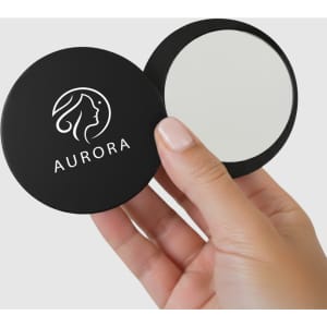 A compact mirror in a black case is being held, featuring a logo on the cover and a reflective surface inside.