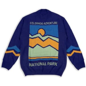 A blue knitted jumper featuring a mountain design with orange and yellow accents, and a branding logo.