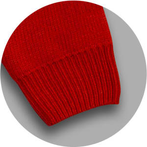 A red knitted jumper featuring a ribbed cuff detail and a solid texture. It has a logo on it.