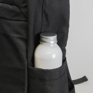A black backpack pocket holds a silver-capped drink bottle, featuring a textured fabric design.
