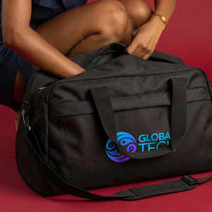 A black duffle bag with handles and a logo, held by a person, set against a red background.