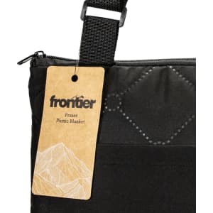 A black picnic blanket with a carrying strap and a tag featuring a brand logo.