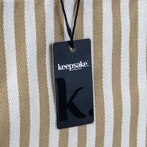 A striped beach tote bag in cream and tan, featuring a tag with a logo attached.