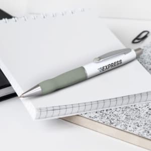 A metal pen with a white barrel and grey grip, placed on a notepad among other stationery items.