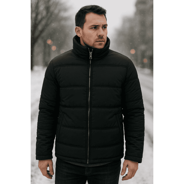 A man is wearing a black padded jacket, standing outdoors in a snowy urban setting.