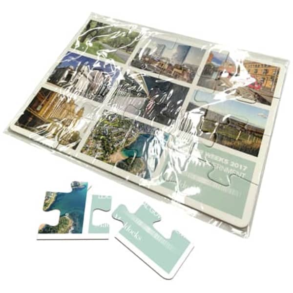 A5 cardboard jigsaw featuring colourful images of landscapes and cityscapes, packaged in clear plastic with puzzle pieces.